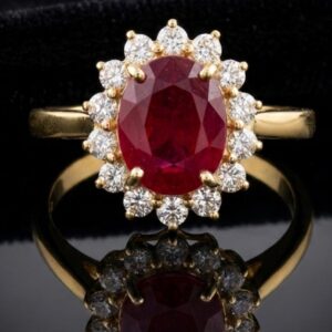 An oval-cut ruby ring set in a gold band, surrounded by a halo of small round diamonds against a black background.